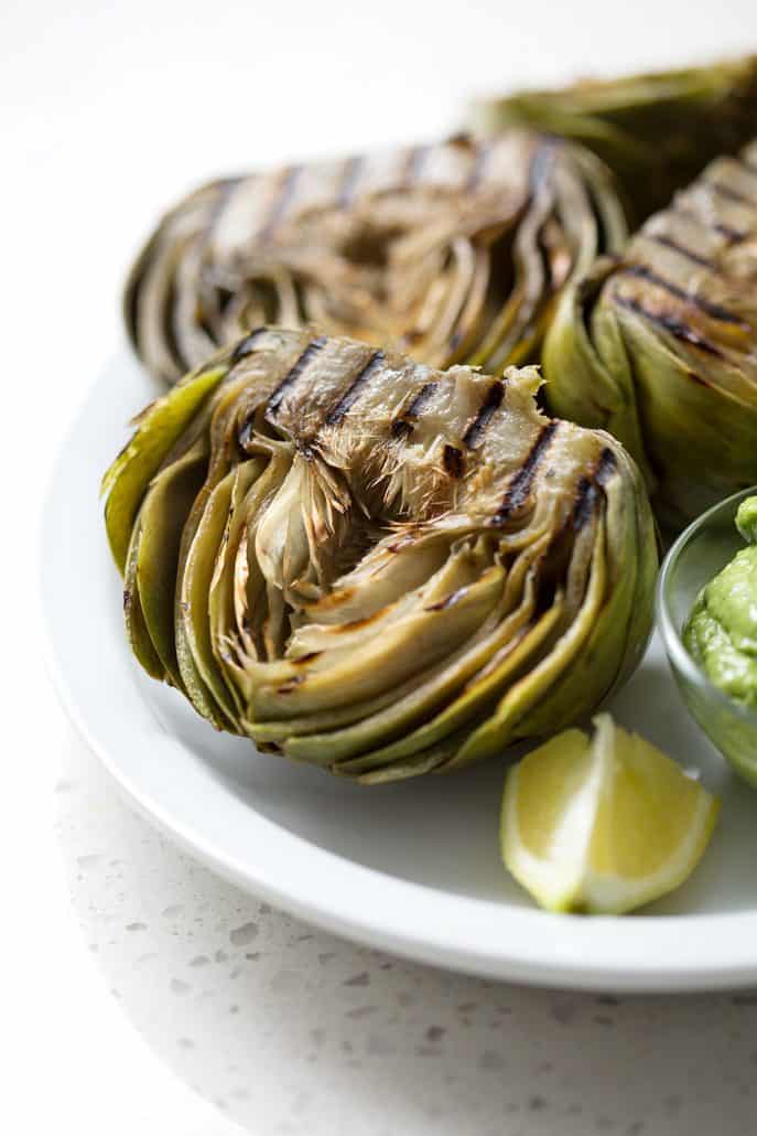 grilled artichokes halved on platter on white background