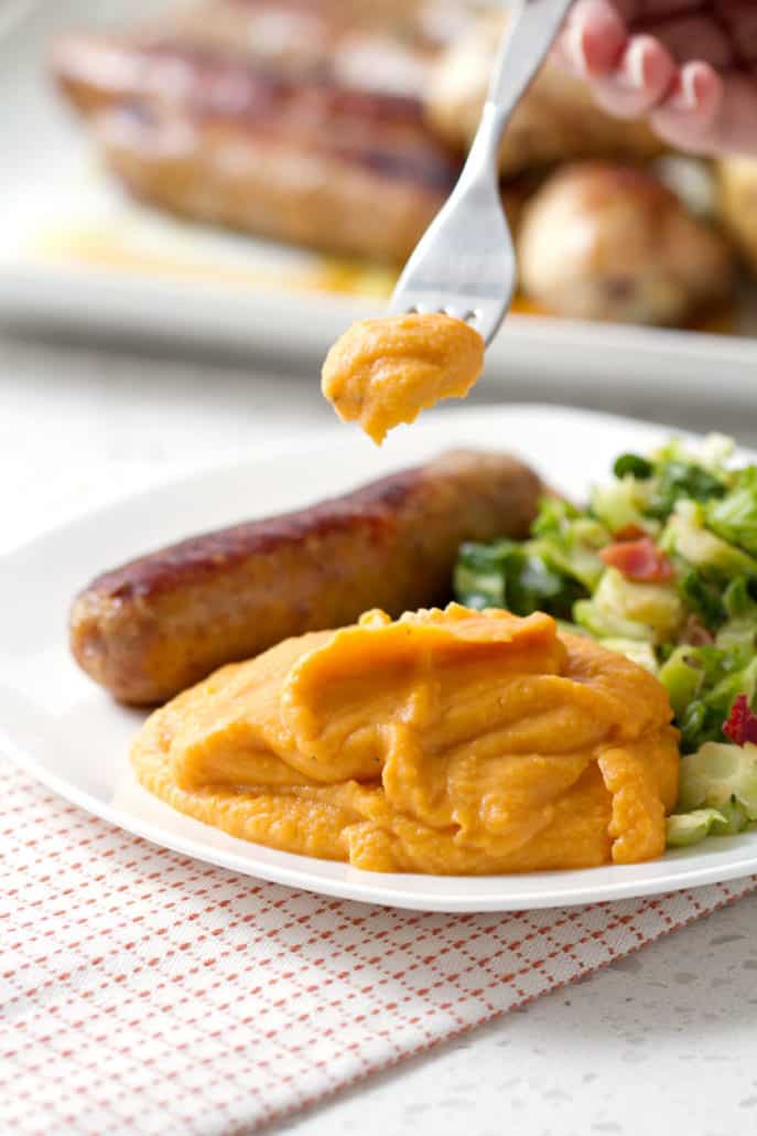 forkful of mashed sweet potatoes with plate of sausage and greens
