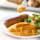 forkful of mashed sweet potato on plate with sausage and greens