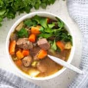 aip beef stew in bowl with spoon surrounded by parsley and towel from above