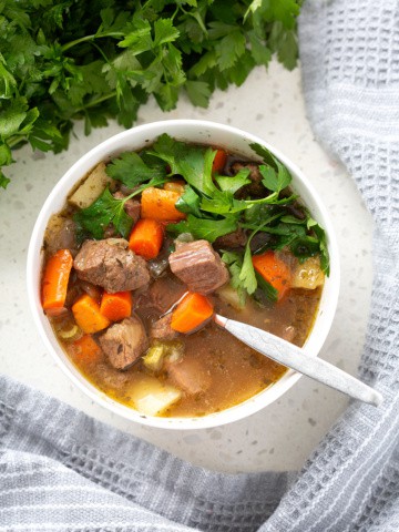 aip beef stew in bowl with spoon surrounded by parsley and towel from above