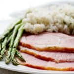 slices of ham on plate with rice and asparagus