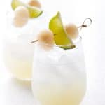 wine glass filled with drink and ice garnished with lime and lychee