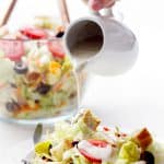 pouring salad dressing over plate of salad on white background