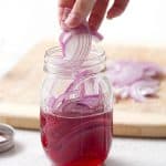adding red onions to a mason jar for pickling