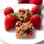 strawberry rhubarb crumble bars on white plate with strawberries