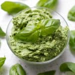 bowl of pesto surrounded by basil leaves