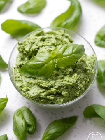 bowl of pesto surrounded by basil leaves