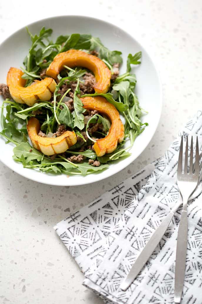 bowl of salad with squash next to a napkin and silverware