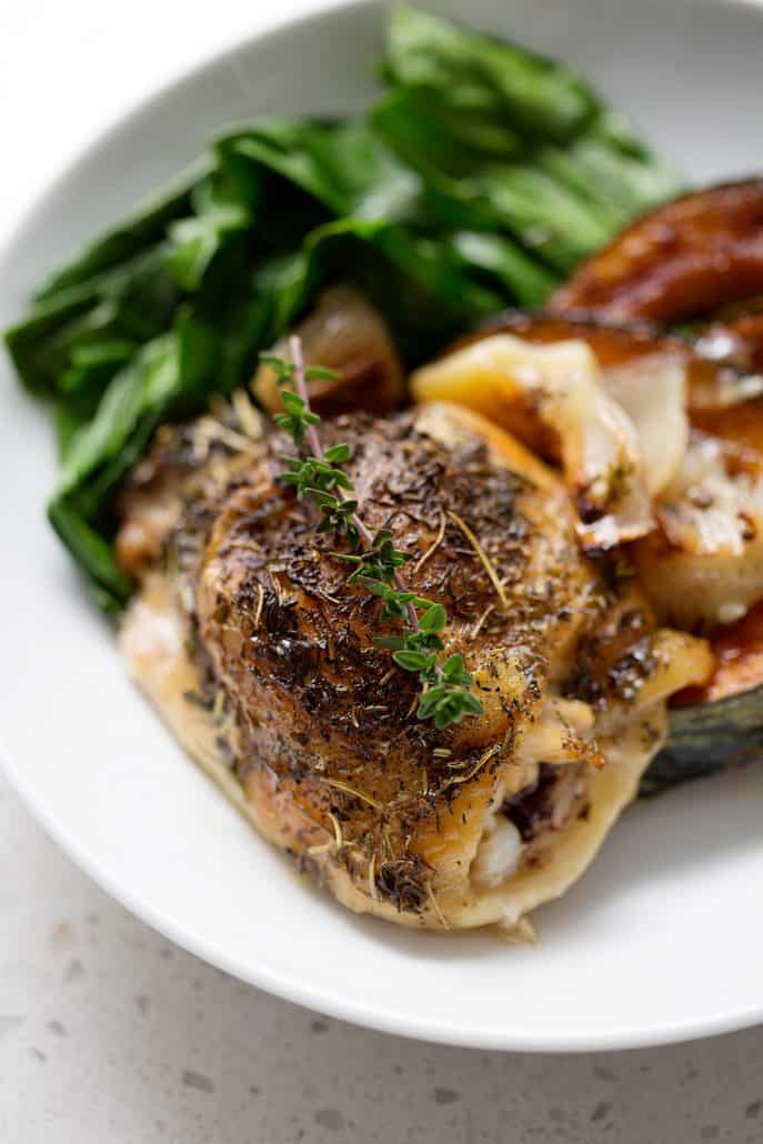 roast chicken garnished with thyme sprig on a plate with greens