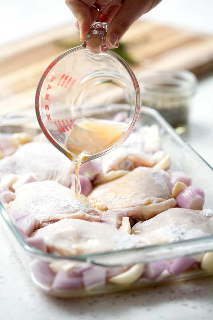 pouring chicken broth over chicken in roasting pan