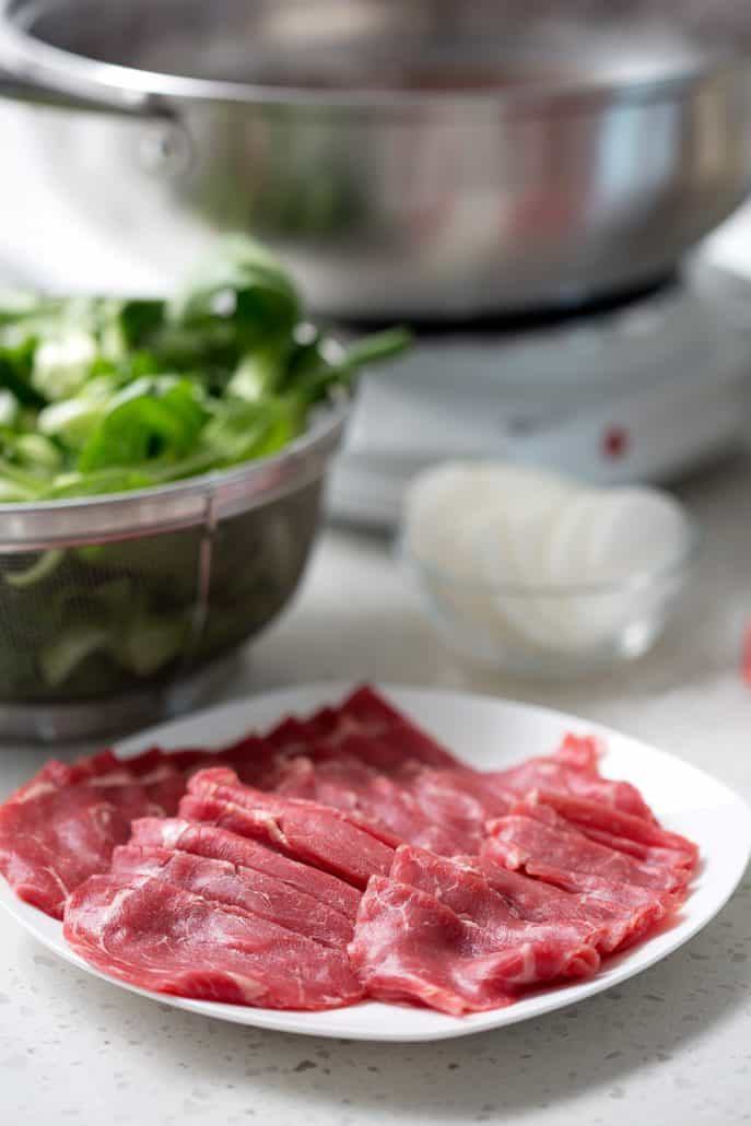 raw meat and bok choy with hot pot pan in the backround