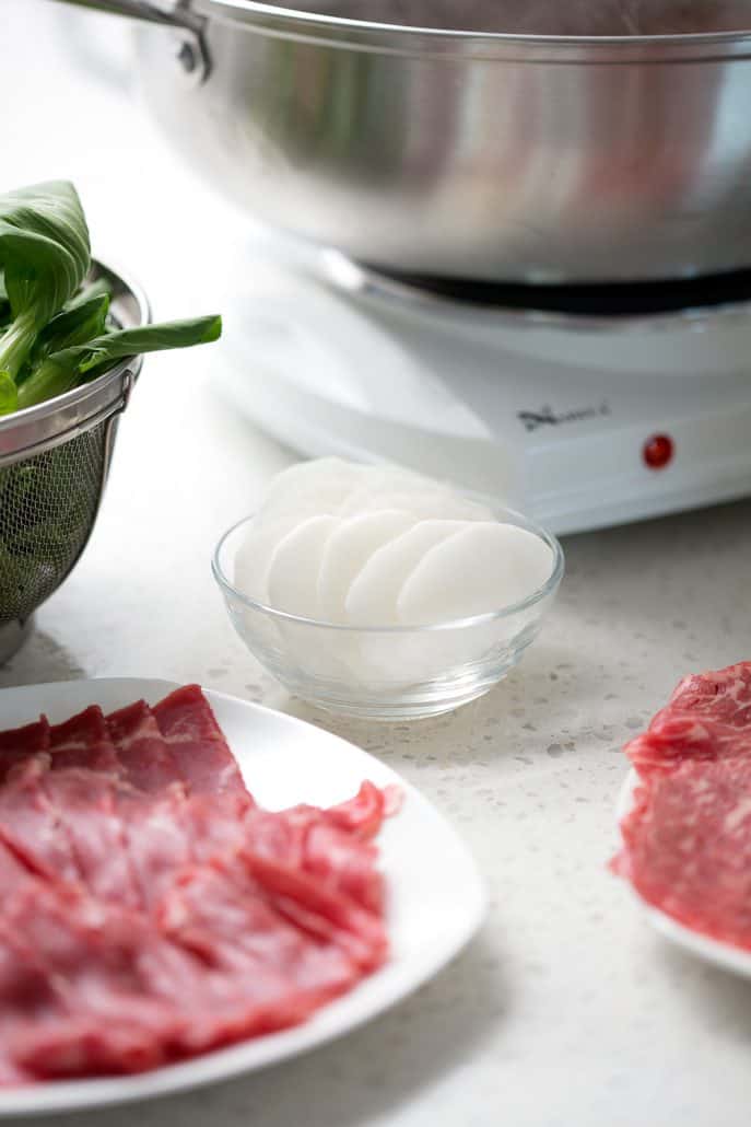 raw meat, daikon and bok choy in front of hot pot pan