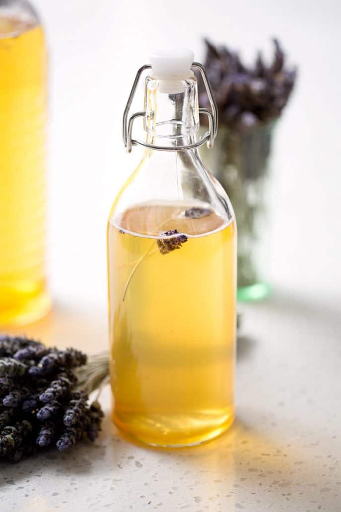 bottle of honey lavender kombucha tea with bunches of lavender on white background