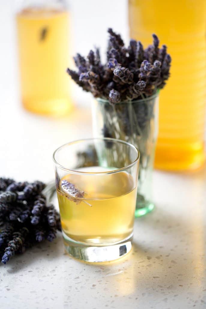 glass and bottle of kombucha tea with bunches of lavender on white background