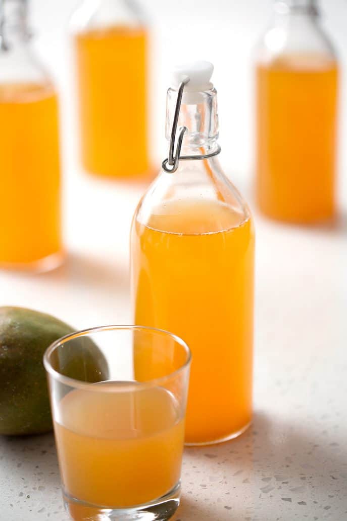 bottle and glass of homemade mango kobucha with mango on white background