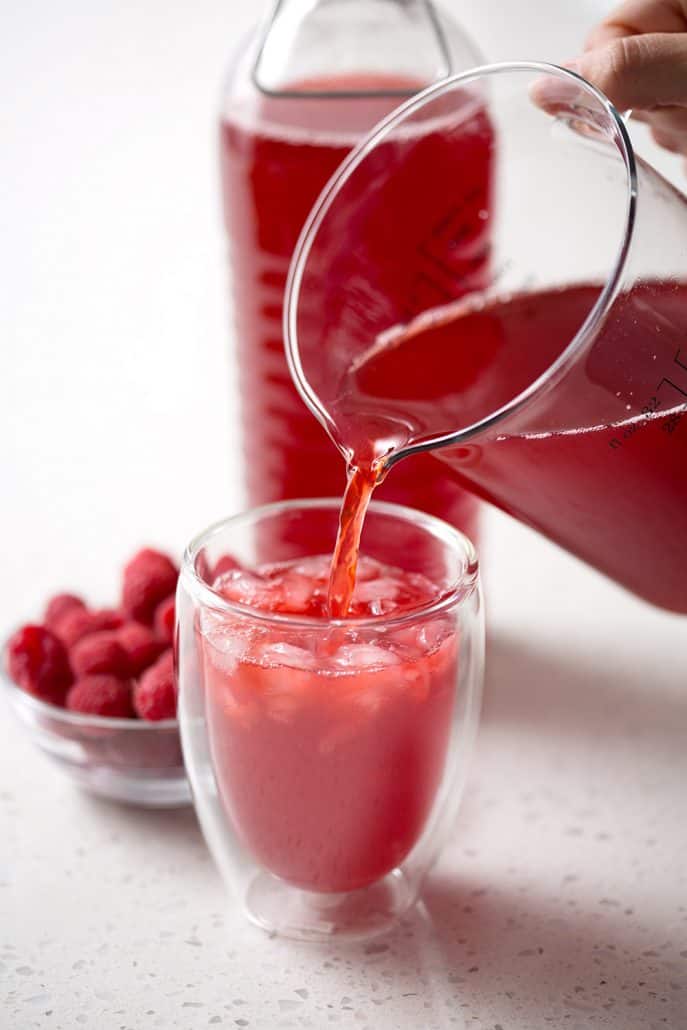 Pouring raspberry thyme kombucha into glass on white background