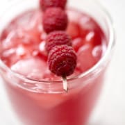 close up of glass of raspberry thyme kombucha with toothpick of fresh raspberries as garnish