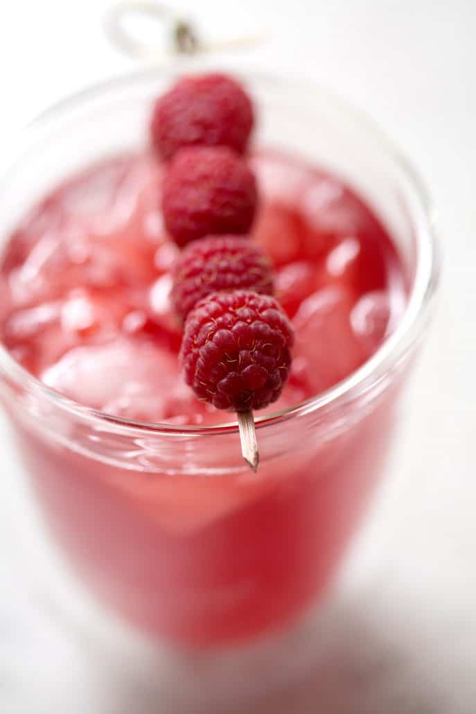 close up of glass of raspberry thyme kombucha with toothpick of fresh raspberries as garnish