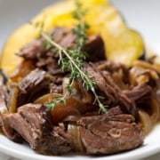 shredded beef on acorn squash with sprigs of thyme on white background