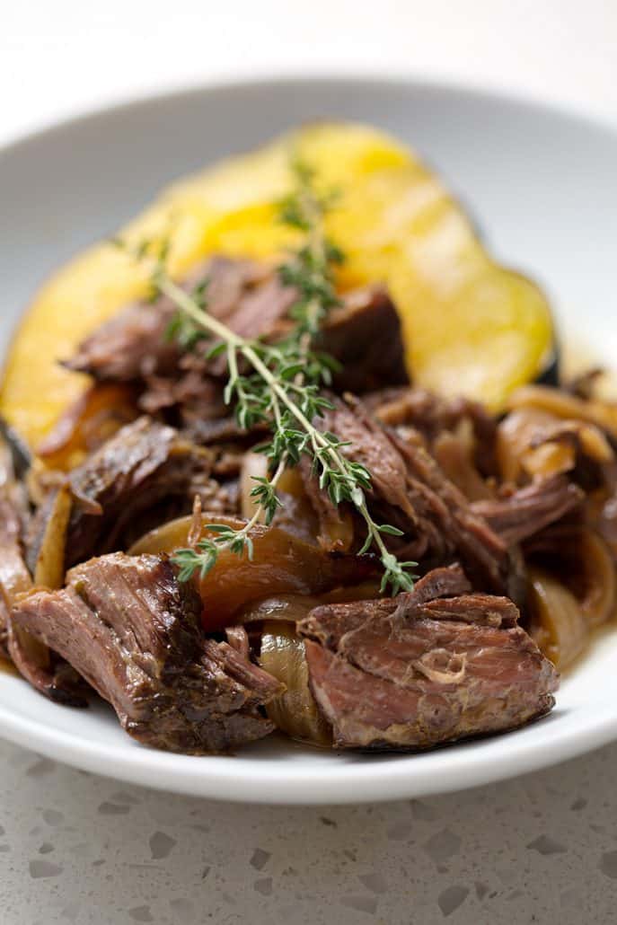 shredded beef on acorn squash with sprigs of thyme on white background