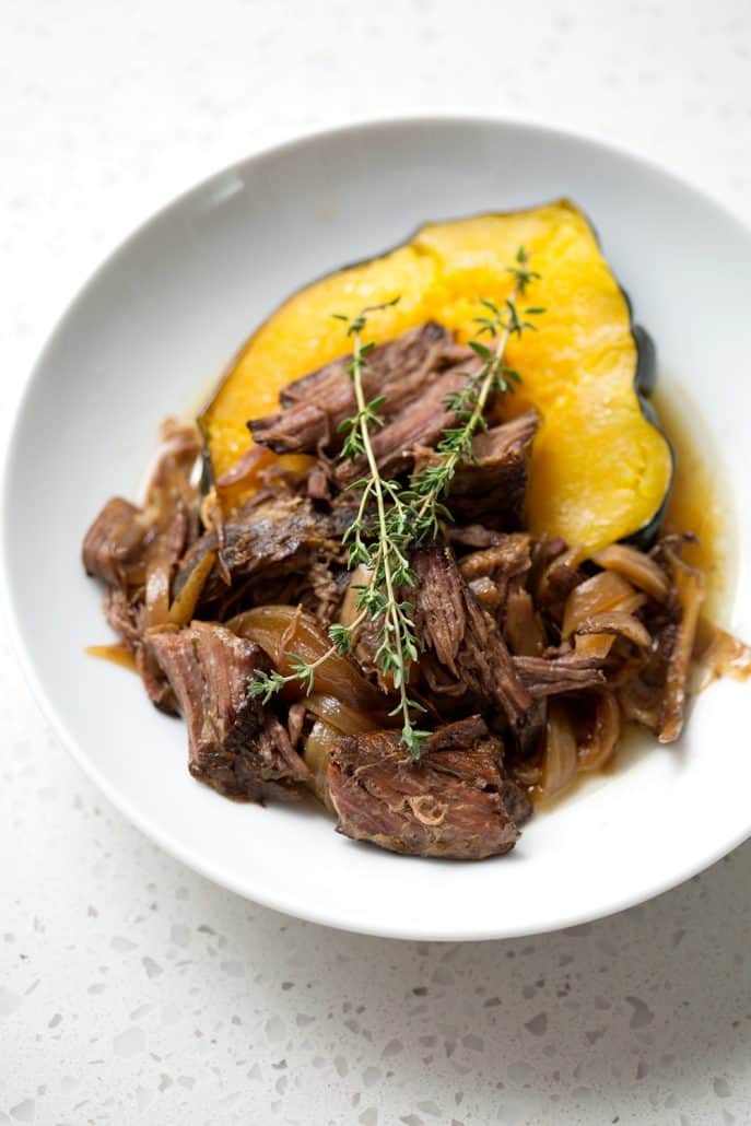 shredded beef on top of acorn squash with sprigs of thyme on white background