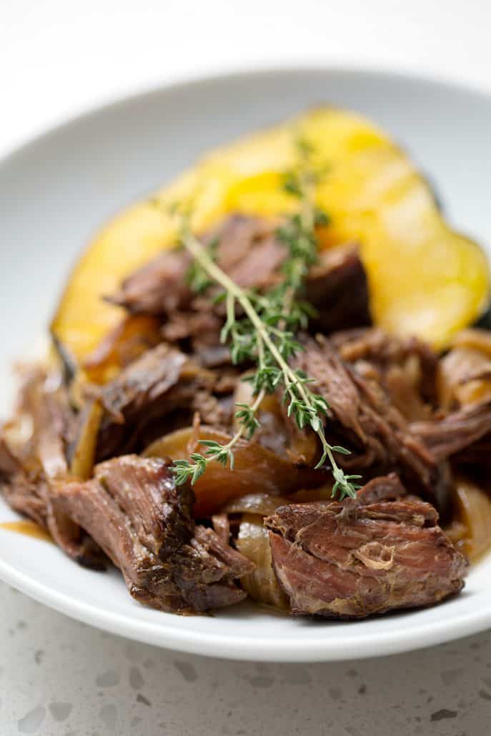 shredded beef on top of acorn squash with sprig of thyme