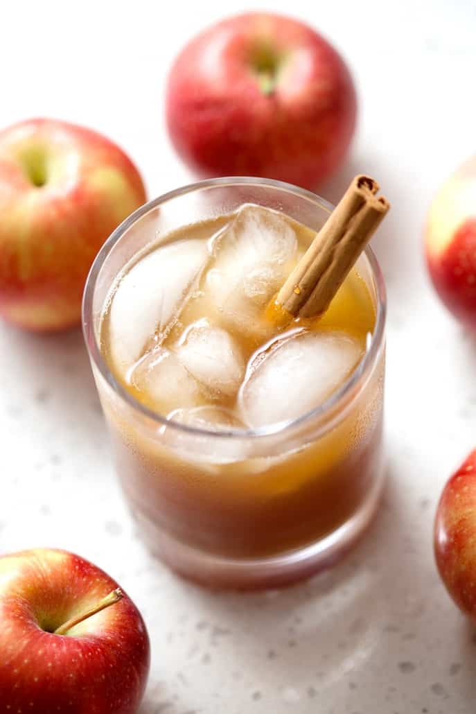 glass of kombucha with cinnamon stick surrounded by apples on white background