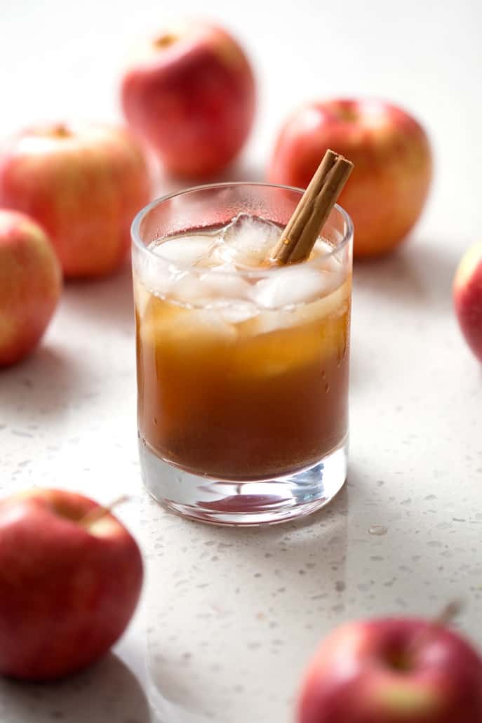 glass of kombucha in glass with apples and cinnamon stick on white background