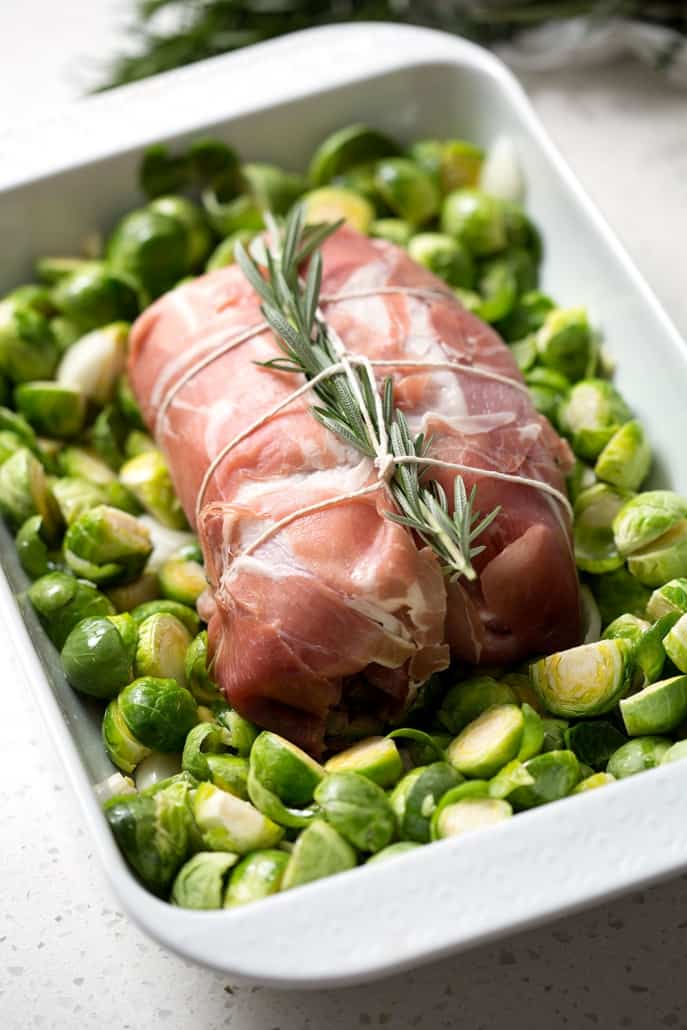 prosciutto wrapped roast with sprig of rosemary on brussel sprouts in pan