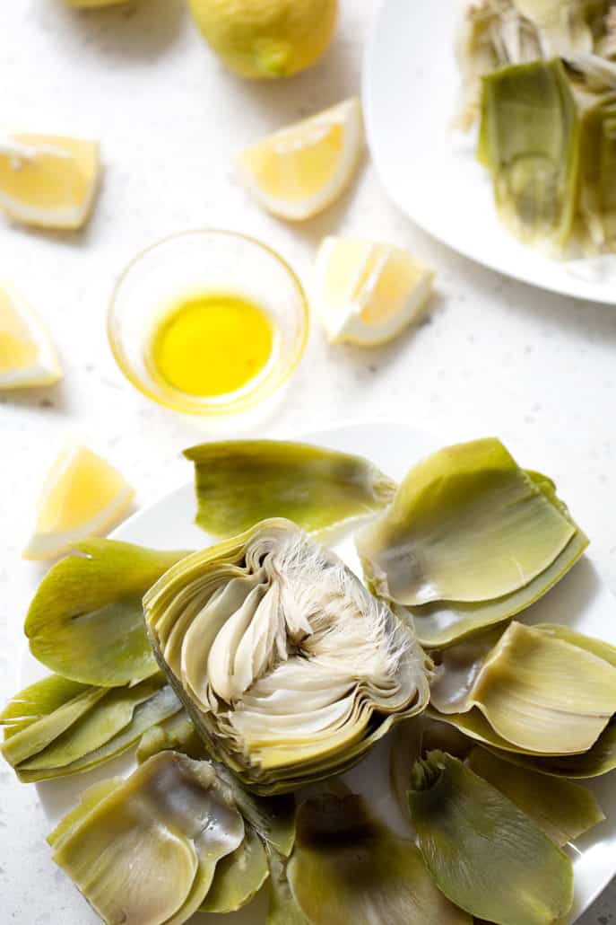 halved artichoke on plate surrounded by leaves and butter dish