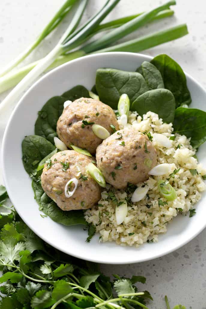 meatballs on bed of cauliflower rice and spinach on white plate 