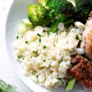 cauliflower rice with herbs in a white bowl with chicken and broccoli