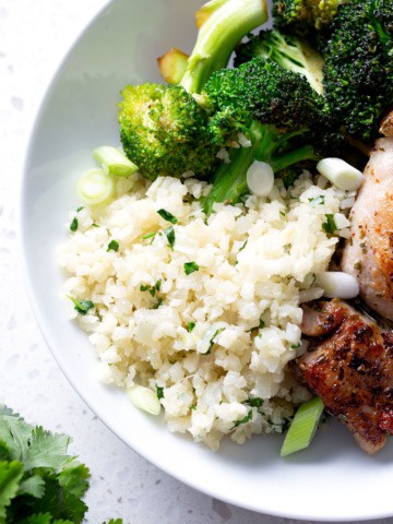 cauliflower rice with herbs in a white bowl with chicken and broccoli