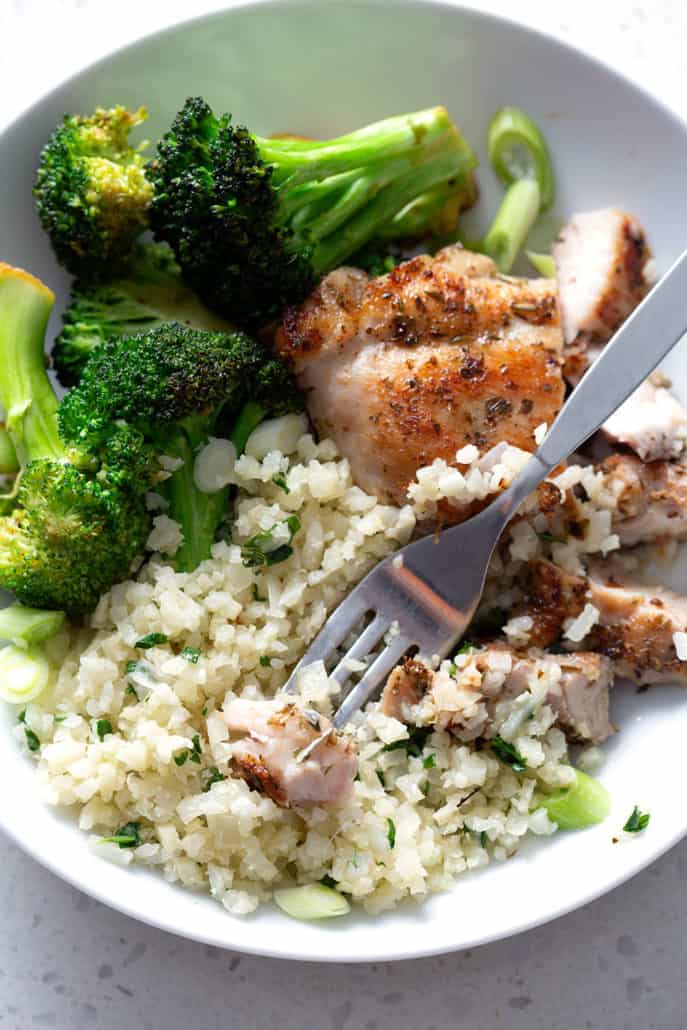 Bite of chicken on fork resting on rice and broccoli