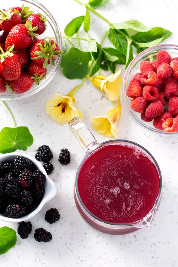 pitcher of juice sitting on white counter with fruit and flowers