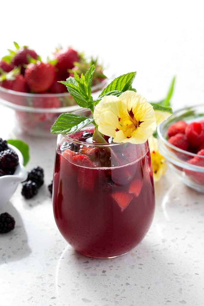 cocktail garnished with mint and flowers on white background