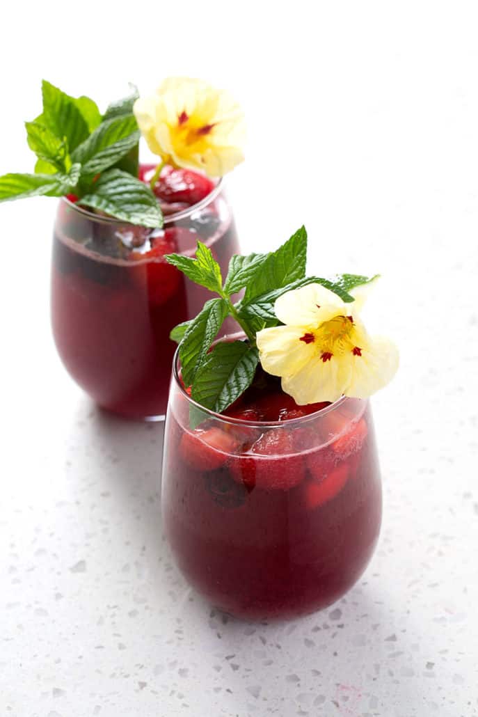 two stemless wine glasses with mint and flower garnishes on white counter