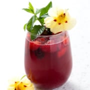 cocktail garnished with mint and flowers sitting on white background