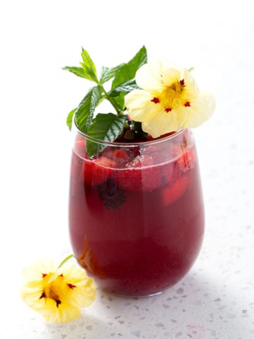 cocktail garnished with mint and flowers sitting on white background