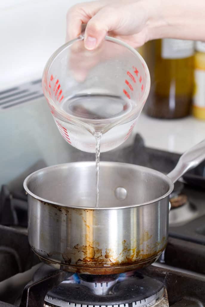 pouring water from measuring cup to saucepan on stovetop