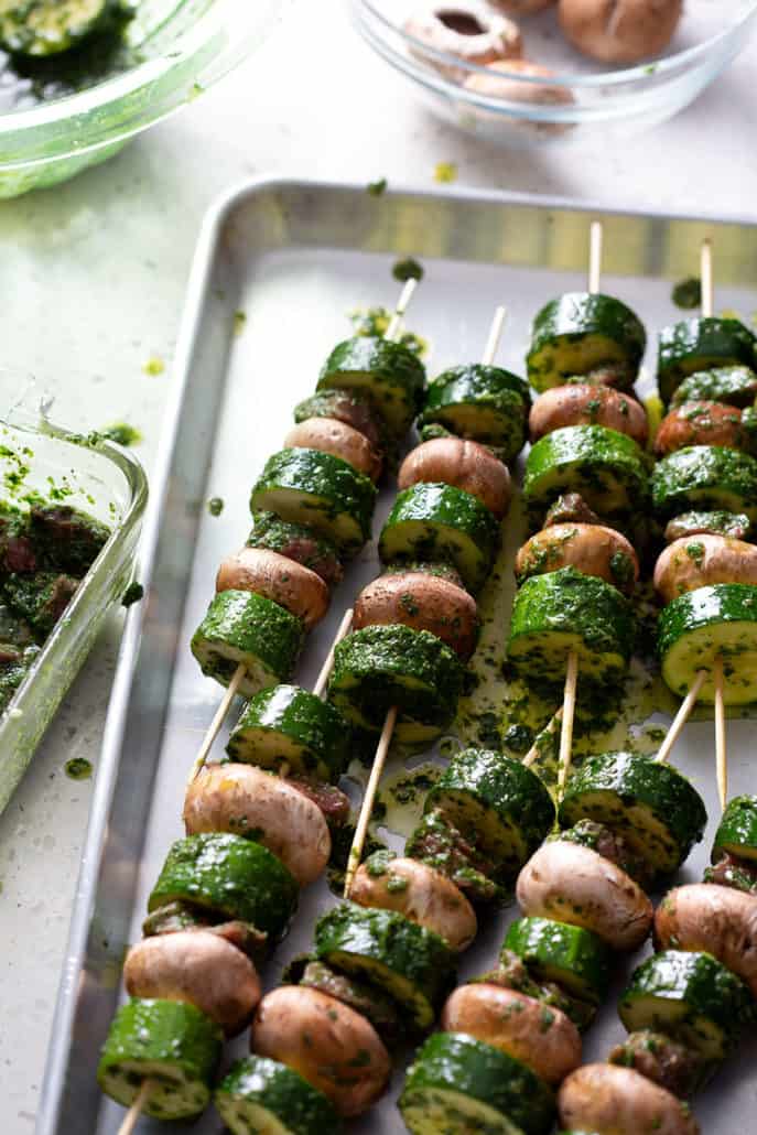 prepping skewers with veggies and meat on baking sheet