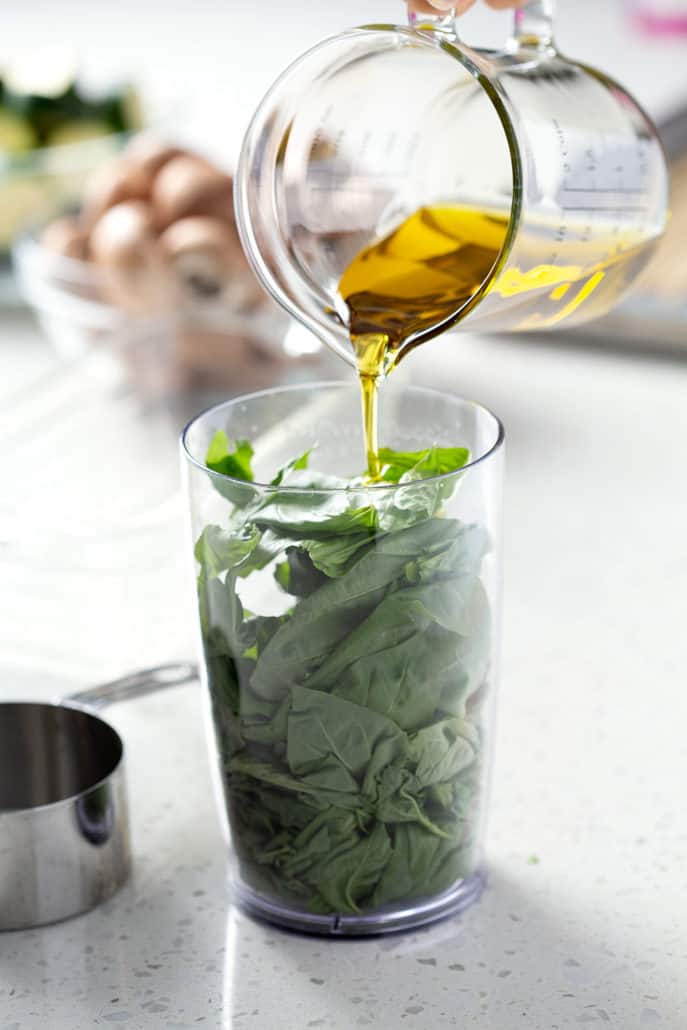 pouring olive oil into container stuffed with basil