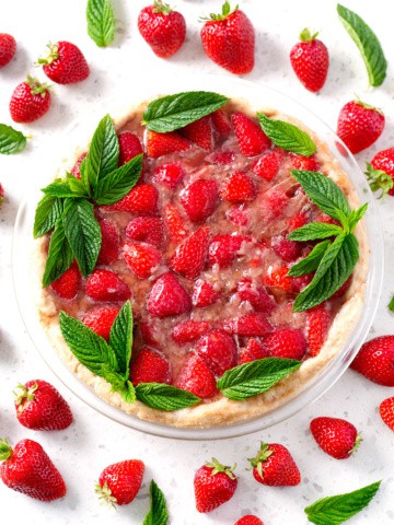strawberry pie decorated with mint on white counter surrounded by strawberries