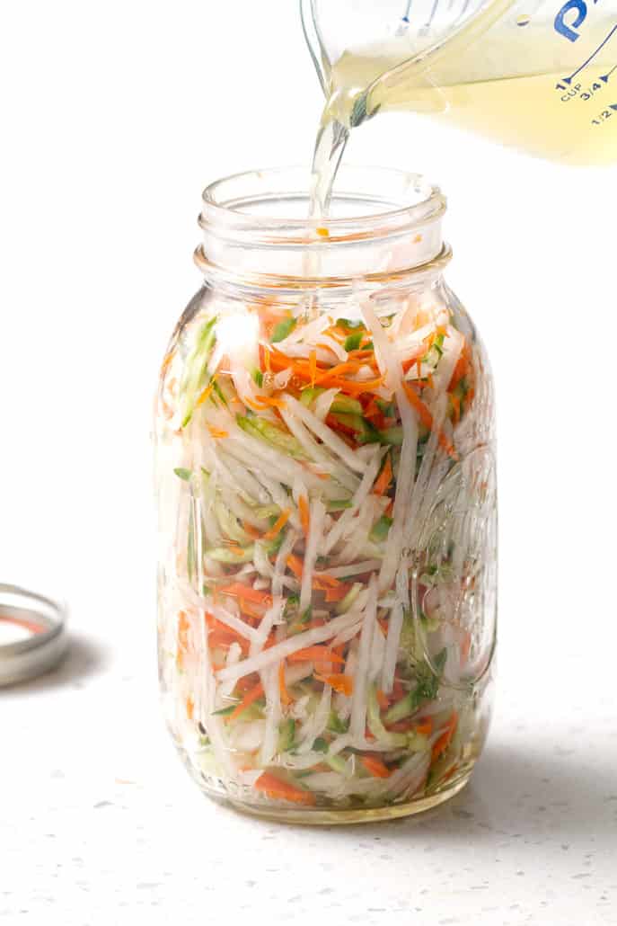 shredded vegetables in large mason jar on white counter