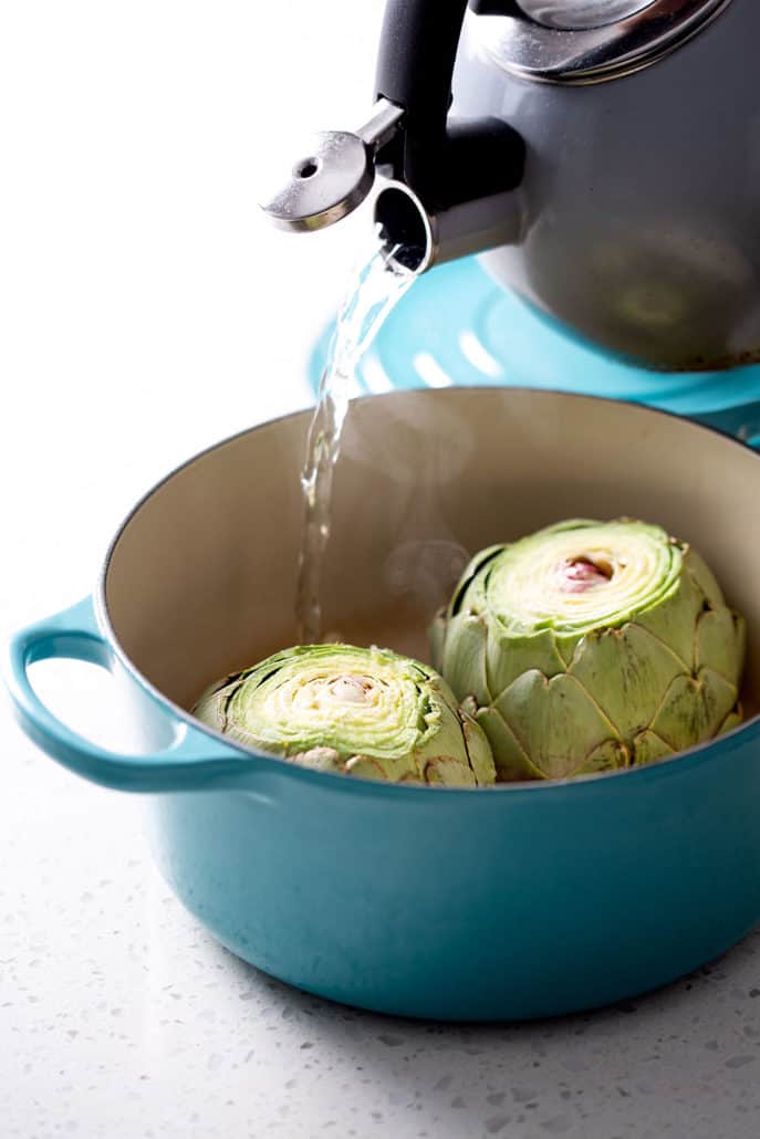 pouring boiling water into artichoke filled dutch oven
