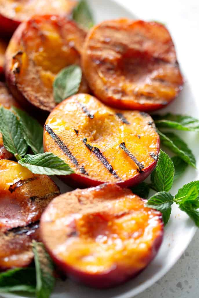 close up of grilled peaches on platter with min garnish
