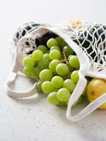 grapes and produce spilling out of a grocery bag on white counter