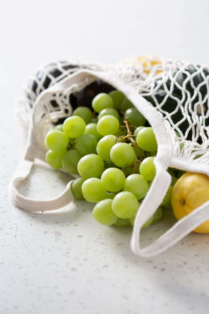 grocery bag with grapes and produce spilling out on white background