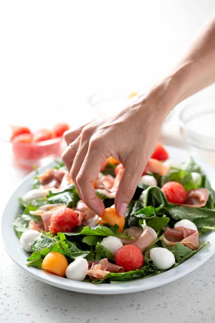 placing ingredients on platter of salad on white background